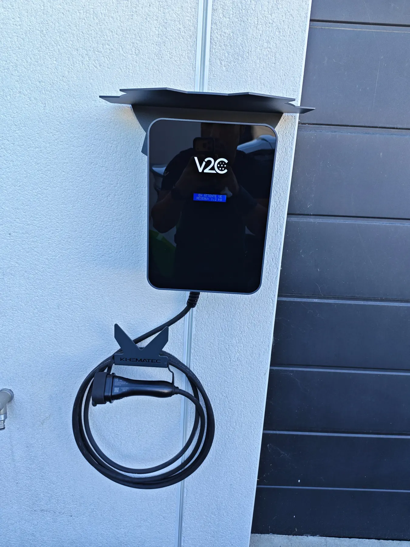 Vue de face d’une borne V2C avec accessoires casquette de protection et support de câble de recharge signés KHEMATEC