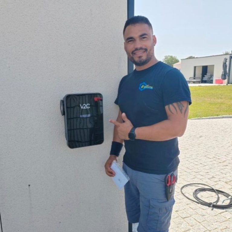Homme souriant en veste bleue à côté d'une borne de recharge électrique.