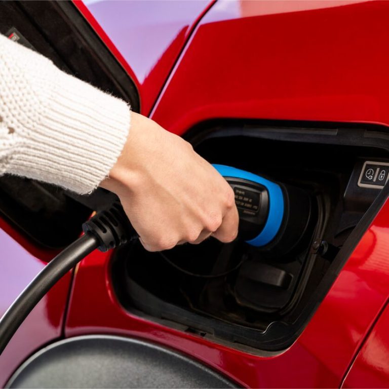 Une main branche un chargeur électrique dans une voiture rouge.