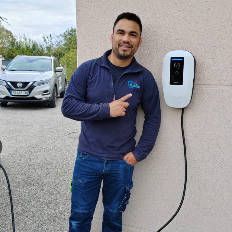 Ronmell Carreras souriant montre une borne de recharge électrique Daze installée sur un mur extérieur.